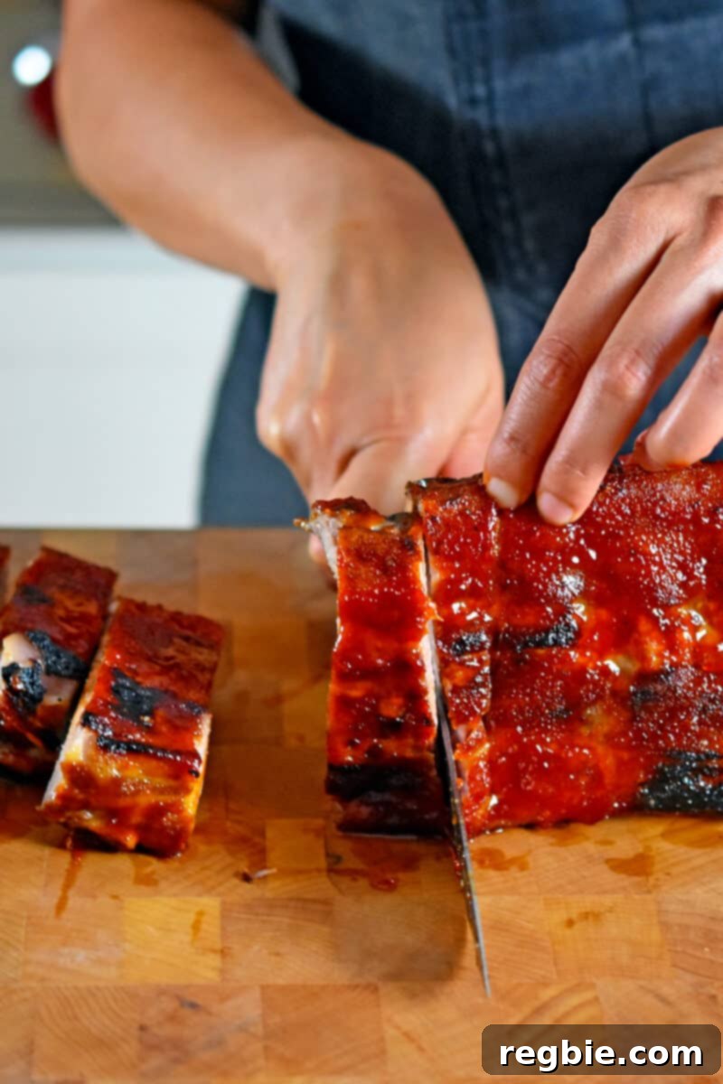Slicing oven baked baby back ribs with a chef's knife on a wooden cutting board.