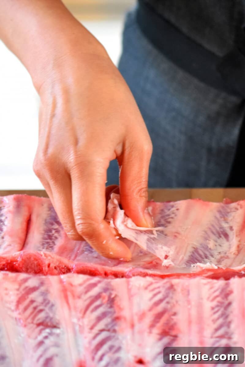 A hand is peeling off the silver skin on the bone-side of the ribs.