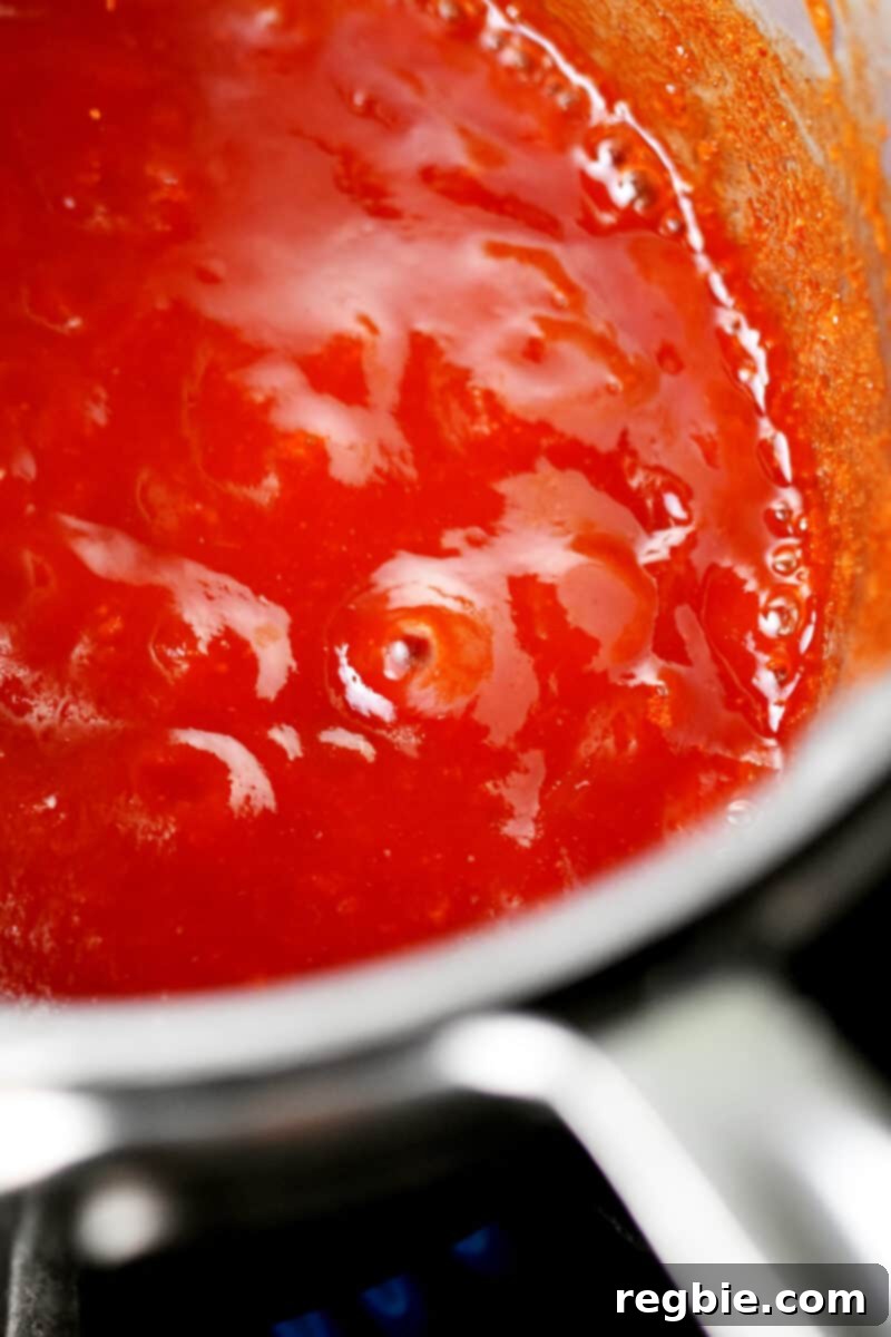 A bubbling red Whole30 barbecue sauce in a stainless steel saucepan.