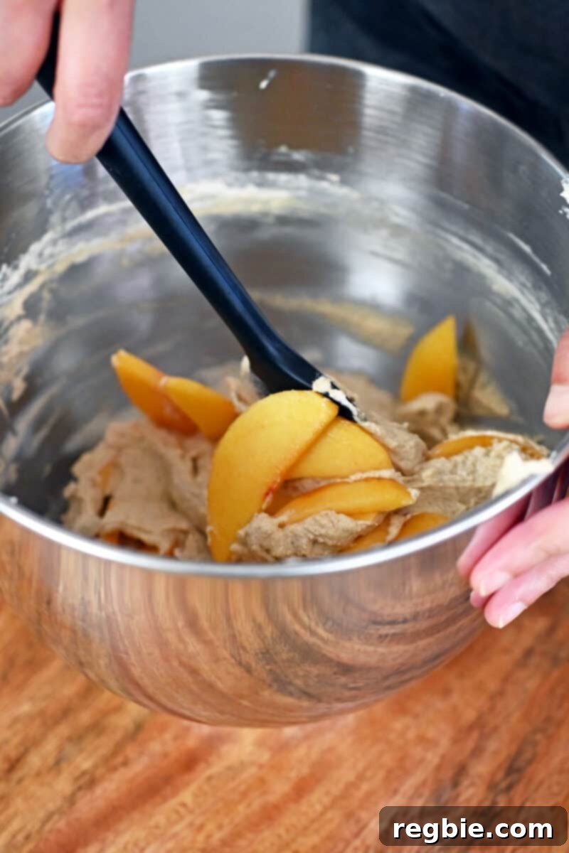 Peach Cloud Cake Paleo Gluten Free 15 Folding peach slices into the cake batter with a black silicone spatula.