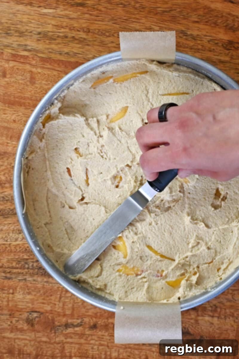 Peach Cloud Cake Paleo Gluten Free 16 An overhead shot of someone using an offset spatula to smooth the top of an unbaked paleo peach cake.