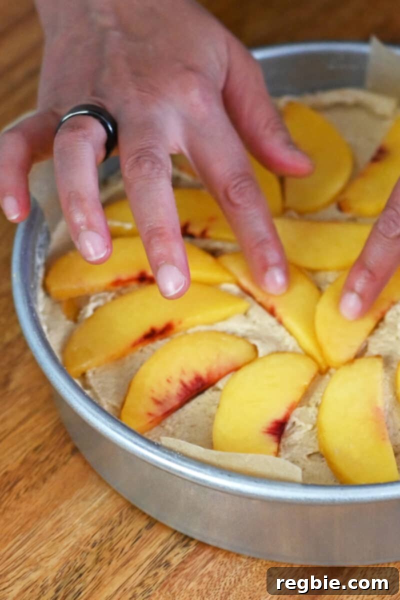 Peach Cloud Cake Paleo Gluten Free 17 A hand is arranging peach slices on top of an unbaked cake.