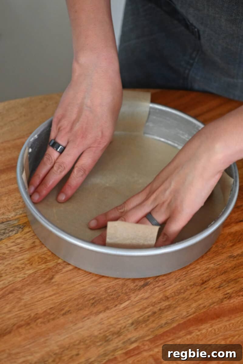 Peach Cloud Cake Paleo Gluten Free 8 Two hands are pressing a piece of parchment paper into a greased round cake pan.