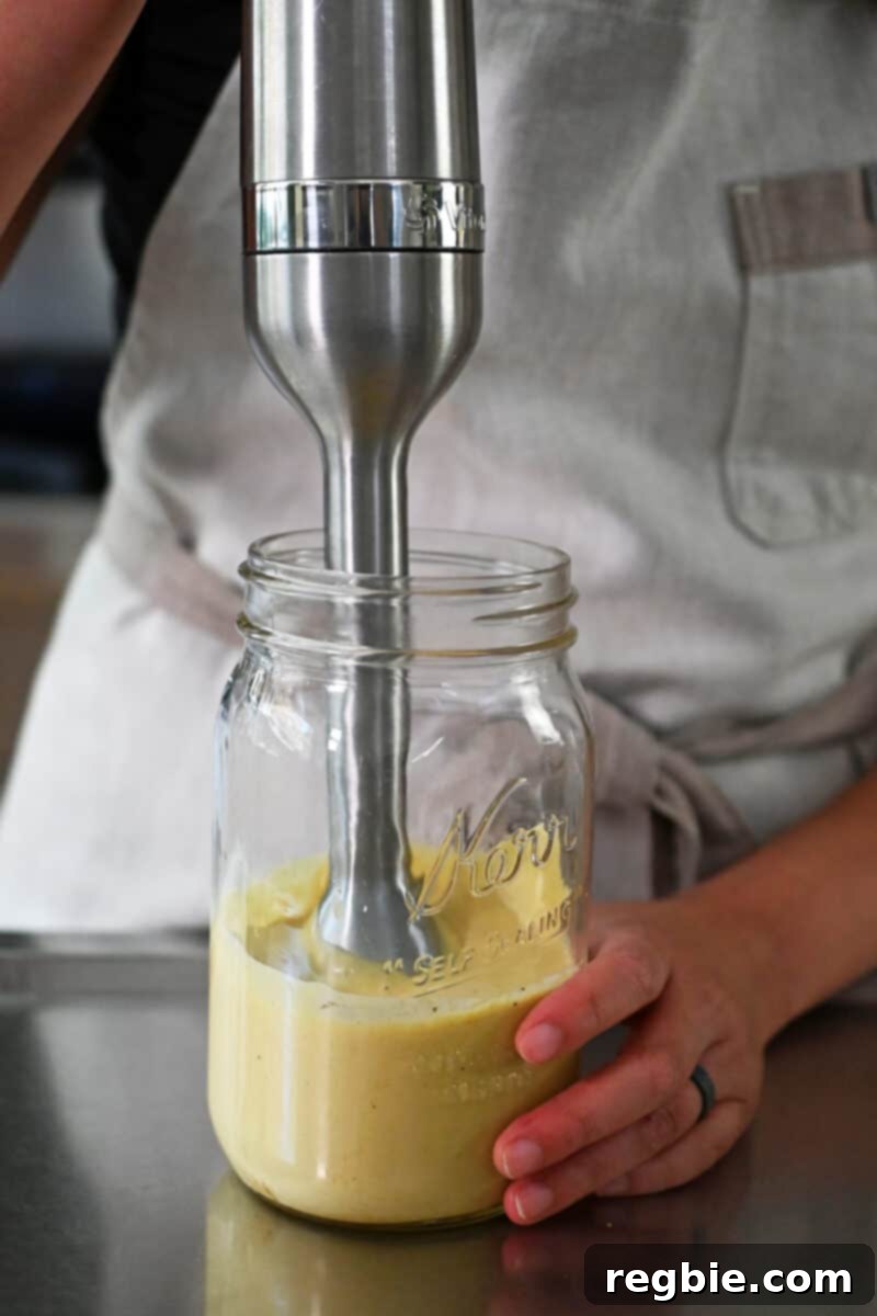 Creamy Dairy Free Caesar Dressing Whole30 Keto 6 An immersion blender actively mixing dairy-free Caesar dressing in a large mason jar, showing the blending process in action.