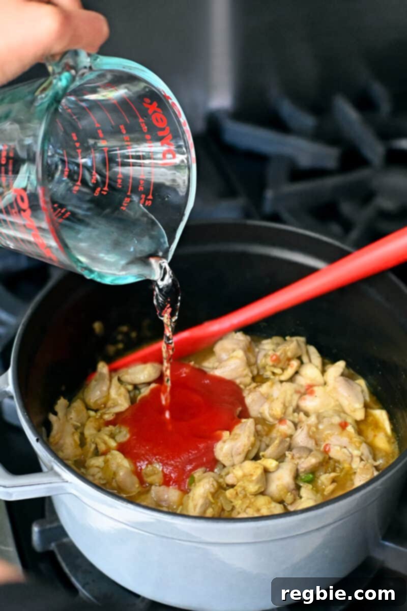 Healthy Instant Pot Chicken Saag Whole30 Keto 14 Pouring water into a large pot filled with chicken, spices, and tomato puree.