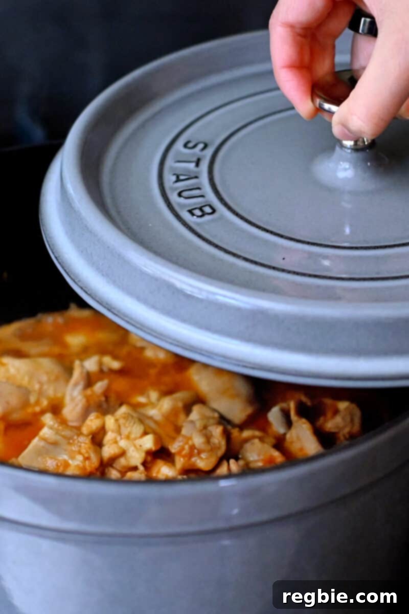 Healthy Instant Pot Chicken Saag Whole30 Keto 15 Putting the lid on a gray Dutch oven filled with a red colored simmering chicken curry.
