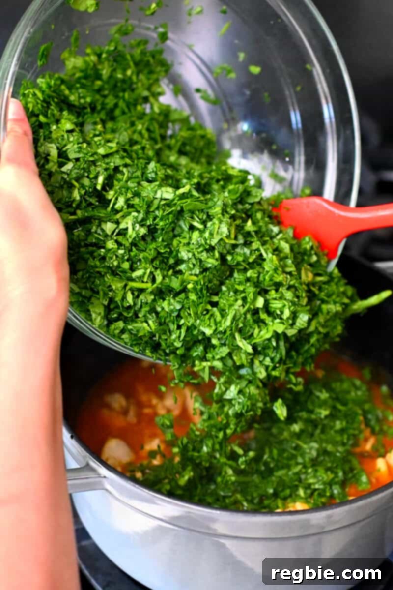 Healthy Instant Pot Chicken Saag Whole30 Keto 16 Adding a big bowl of chopped baby spinach to a pot filled with chicken and tomato curry.