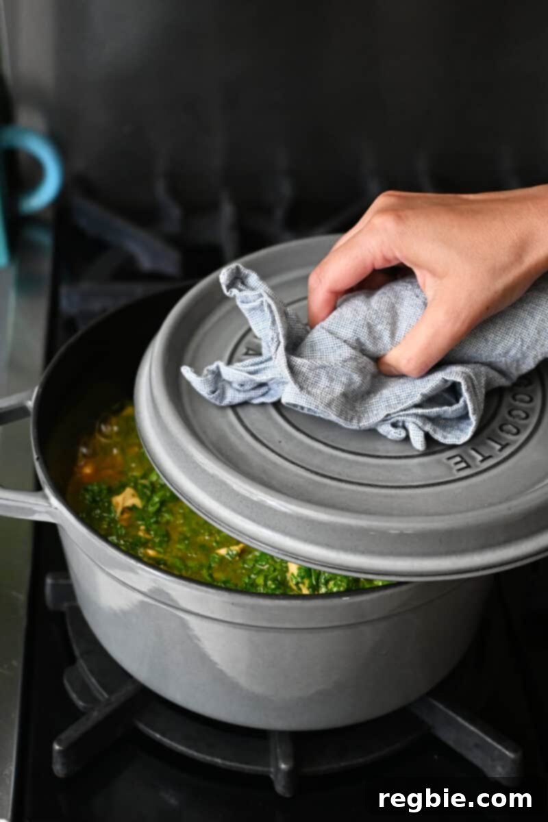 Healthy Instant Pot Chicken Saag Whole30 Keto 17 A hand clasping a cloth is putting the lid on a gray dutch oven filled with chicken saag.