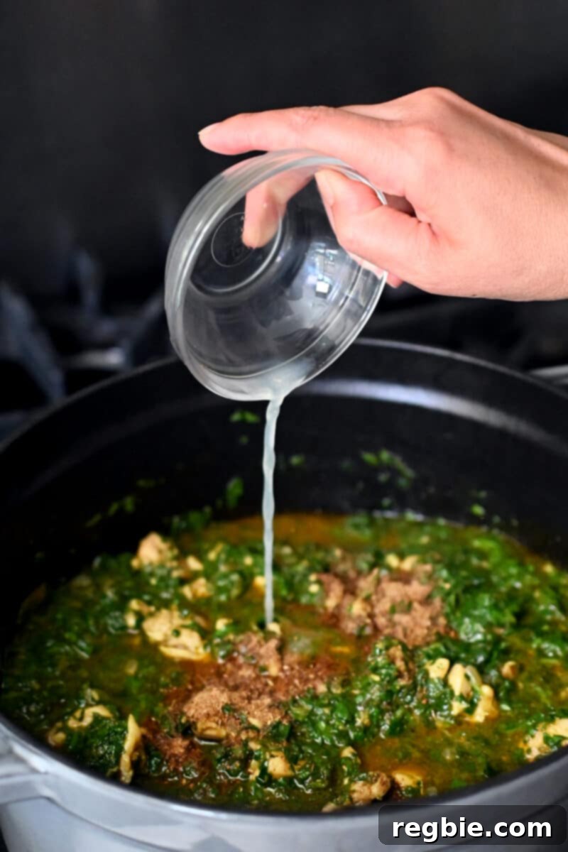 Healthy Instant Pot Chicken Saag Whole30 Keto 18 Pouring a small bowl of lemon juice into a pot filled with cooked chicken saag curry.