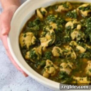 A hand is holding an off-white bowl filled with chicken and spinach Indian curry.