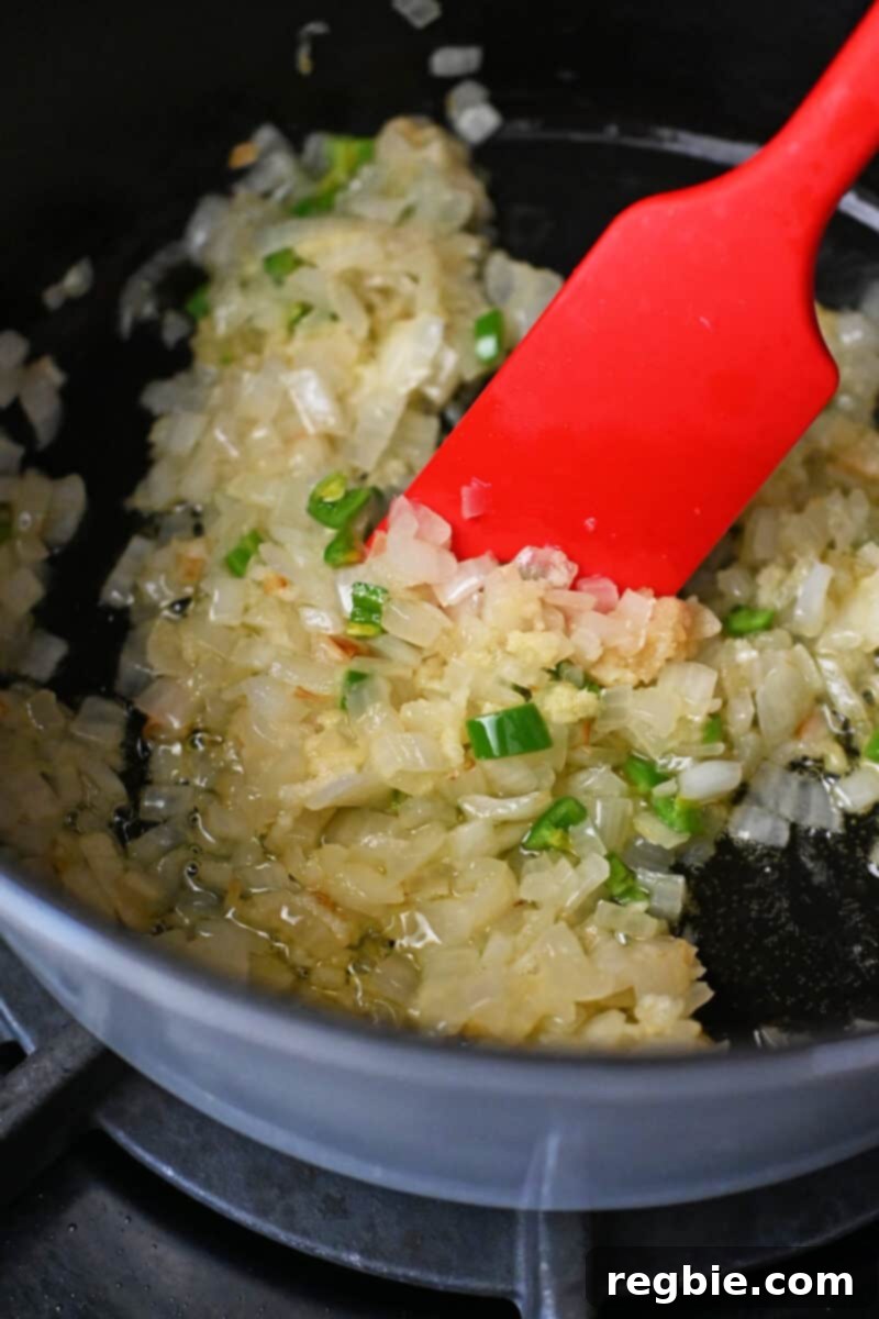 Healthy Instant Pot Chicken Saag Whole30 Keto 9 A red silicone spatula is mixing sautéed chopped onions, minced ginger, minced garlic, and diced green peppers in a pot.