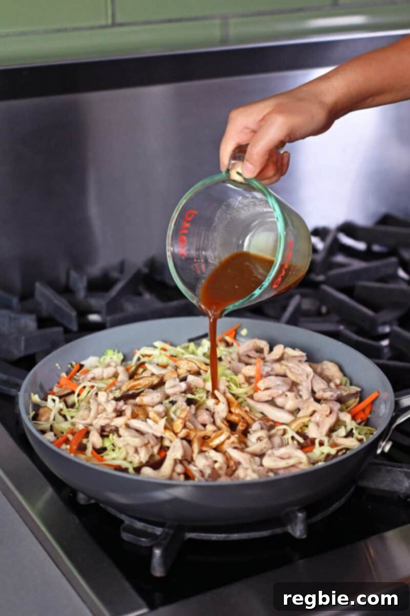 Pouring in the gluten free and paleo sauce to a skillet filled with Moo Shu Chicken, ensuring even distribution and thickening.