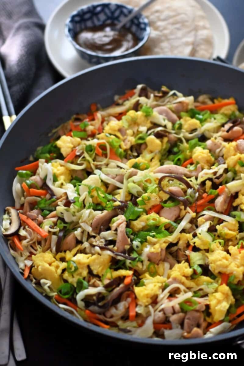 Closeup shot of a skillet filled with moo shu chicken along with paleo hoisin sauce and grain-free tortillas for wrappers, ready for assembly.