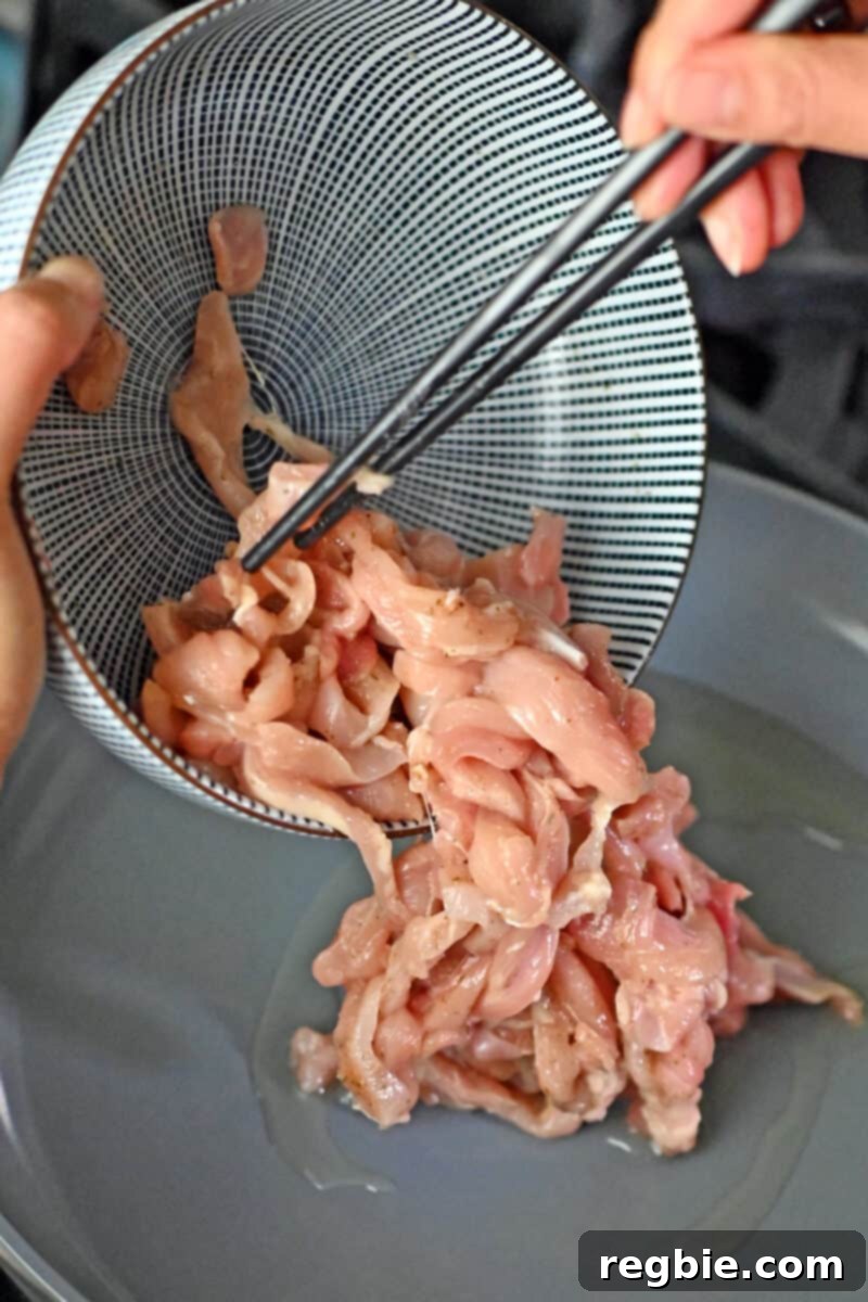 Using chopsticks to add raw seasoned chicken thigh strips to a non-stick pan with hot oil for a quick sear.