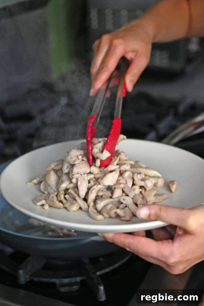 Using a pair of tongs to transfer cooked thinly sliced chicken thighs to a plate for Moo Shu Chicken, keeping it separate from other ingredients.