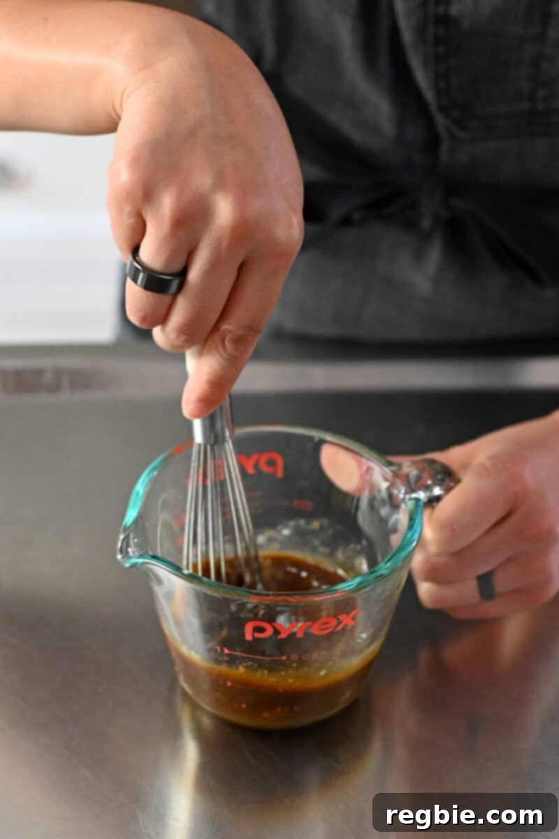 Whisking the sauce for Moo Shu Chicken in a liquid measuring cup, ensuring all ingredients are well combined for a smooth consistency.
