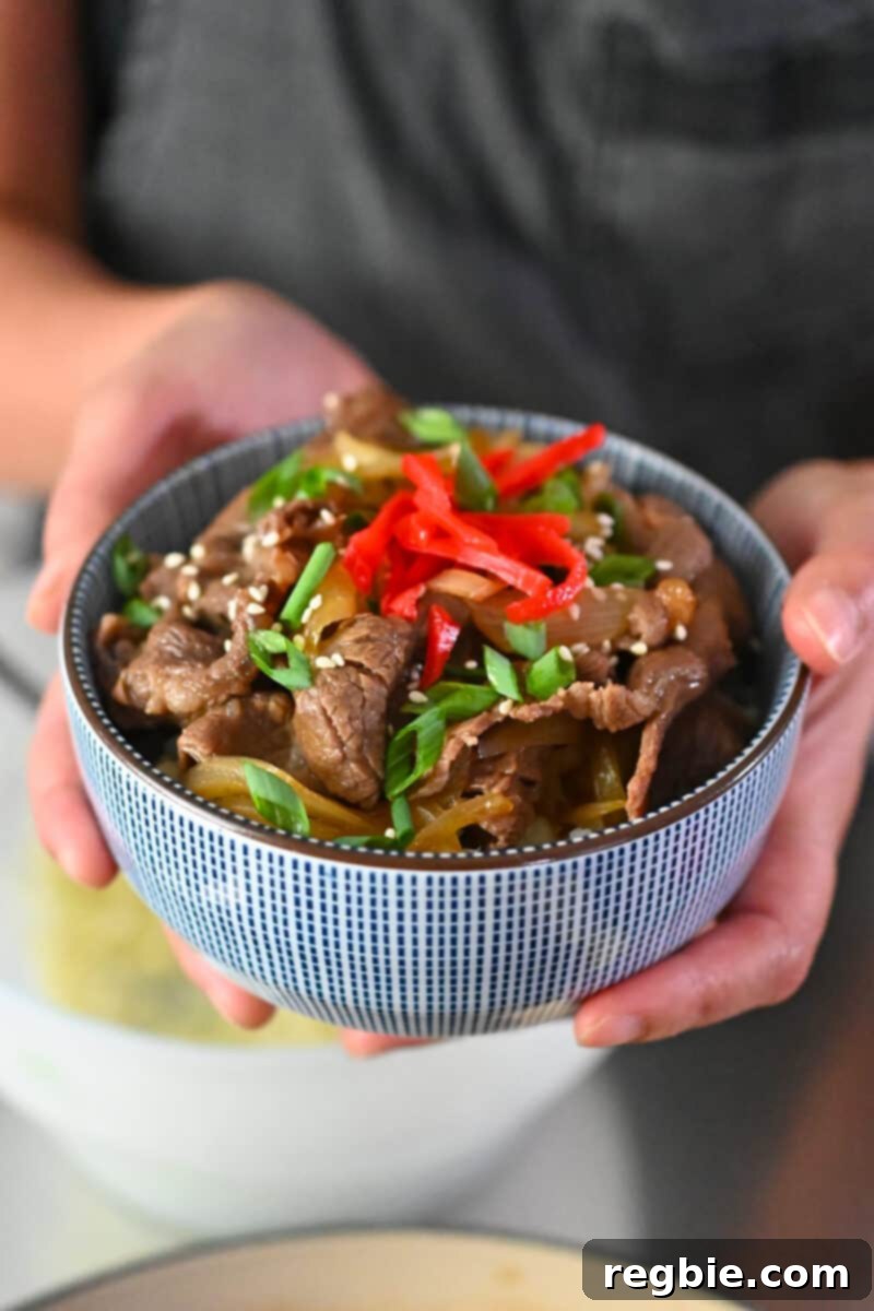 Someone holding a blue and white bowl filled with gyudon, a paleo and gluten free Japanese beef bowl.