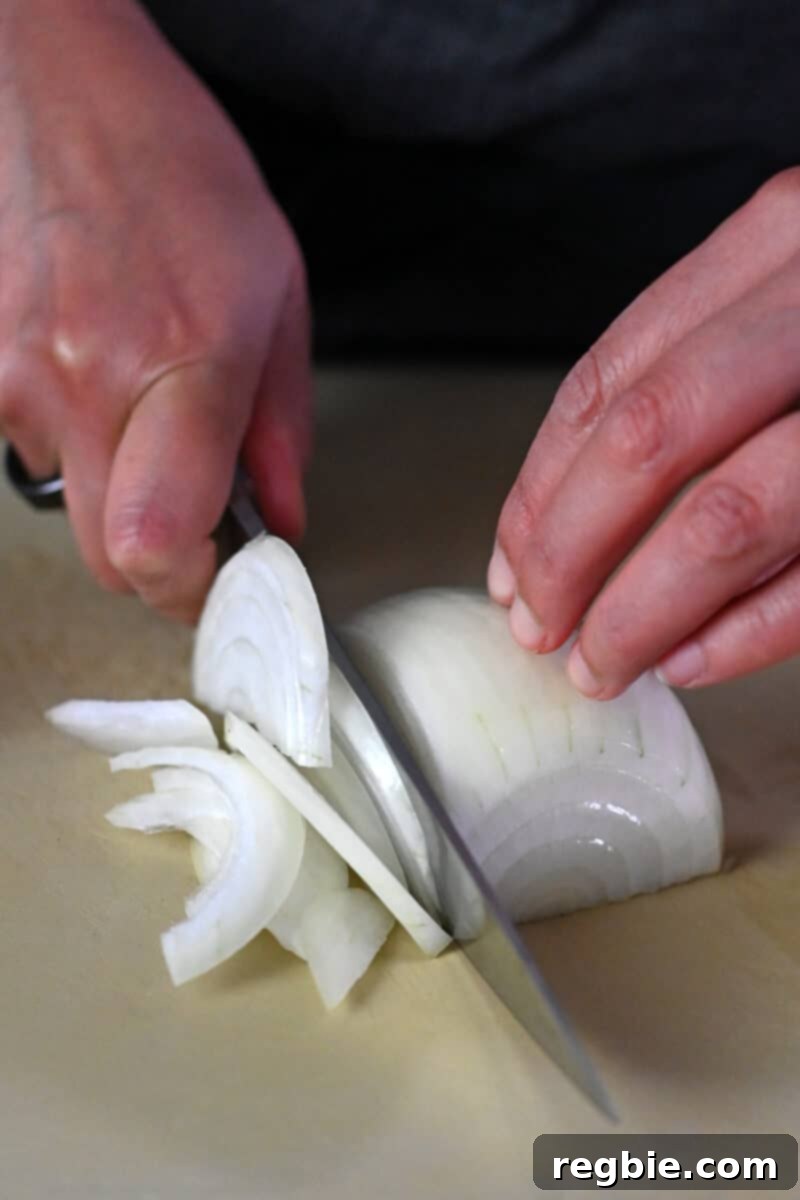 A closeup of a person thinly slicing half a raw onion for healthy gyudon.