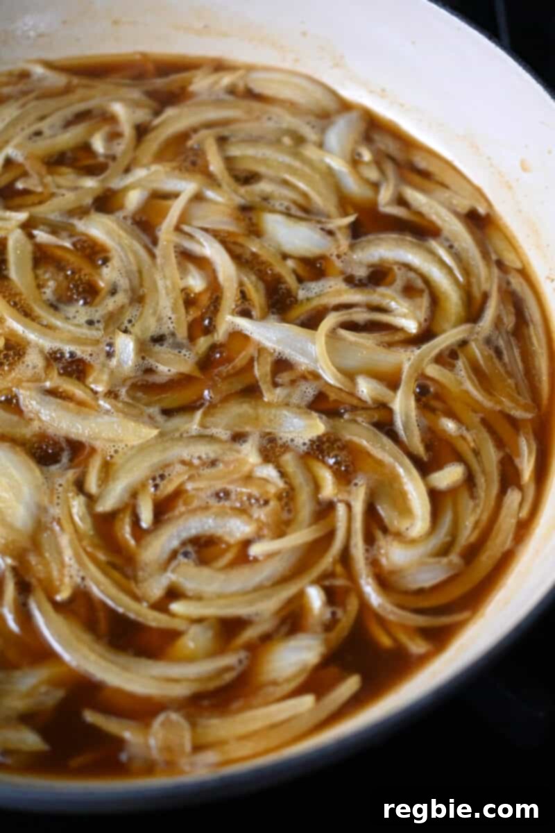 A large enamel cast iron skillet filled with thinly sliced onions in a simmering brown sauce for healthy gyudon.