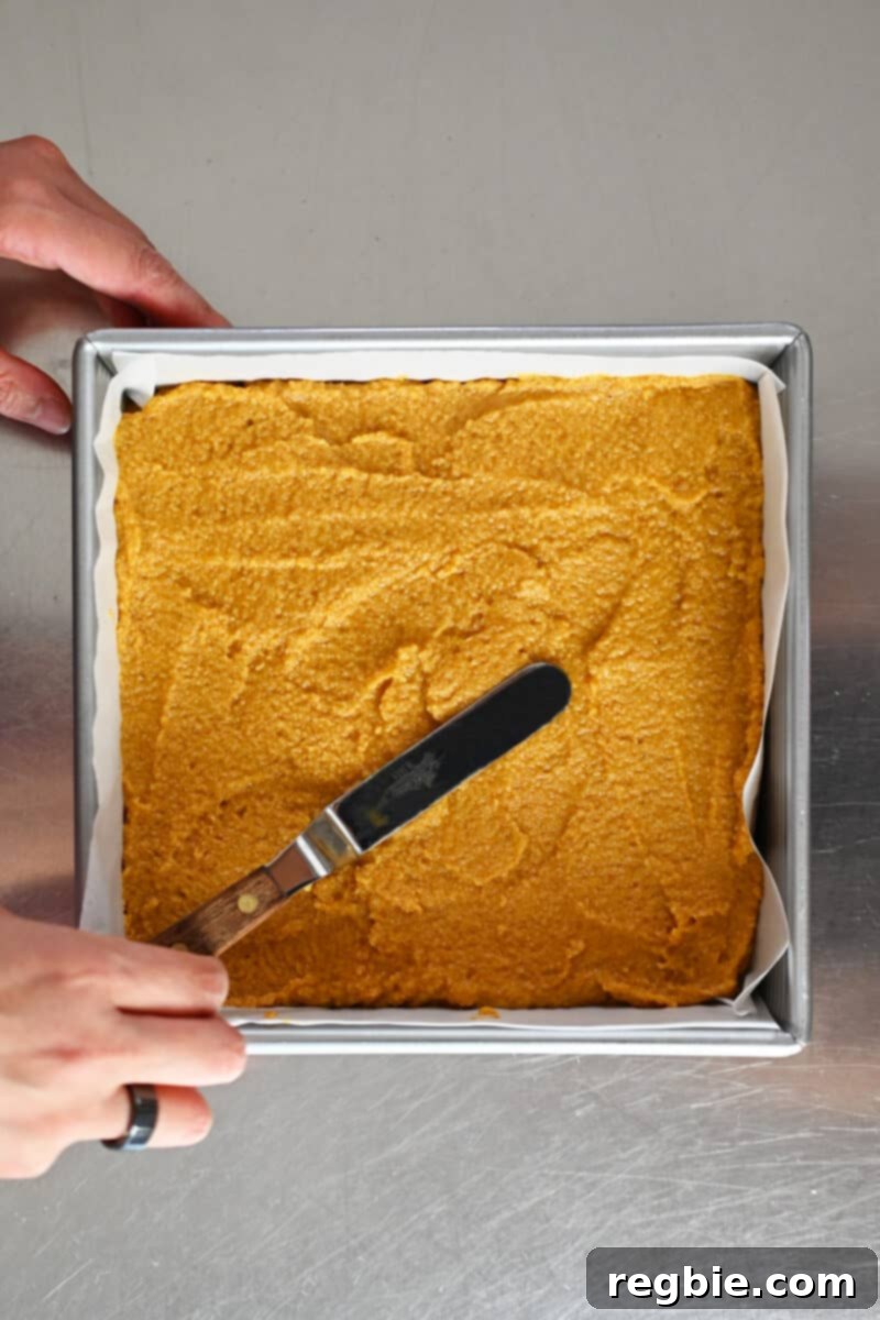 Guilt Free Paleo Pumpkin Bars 11 An overhead shot of an offset spatula delicately smoothing the top of the paleo pumpkin bar batter, preparing it for the oven.