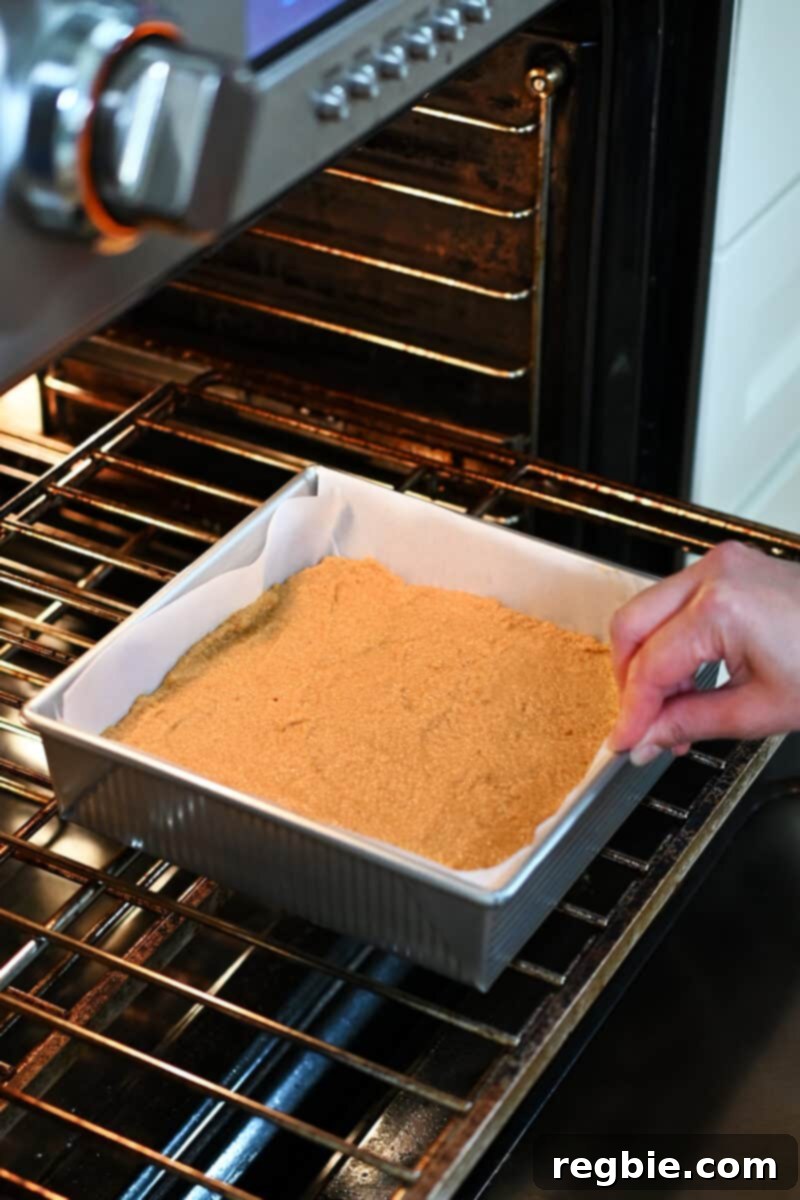 Guilt Free Paleo Pumpkin Bars 12 A hand is carefully placing a square pan filled with paleo pumpkin bars into an open, preheated oven for baking.