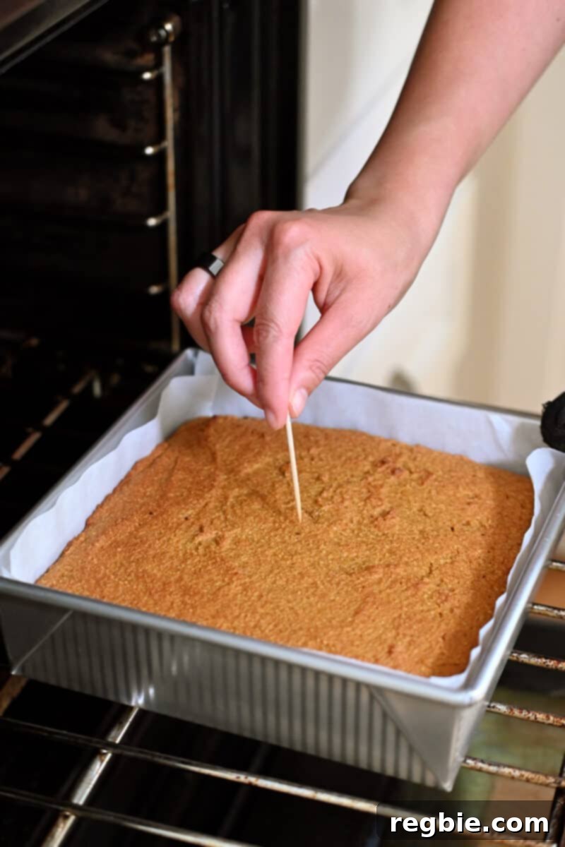 Guilt Free Paleo Pumpkin Bars 13 A toothpick is being inserted into a pan filled with freshly baked pumpkin bars to test for doneness, indicating a perfect bake.