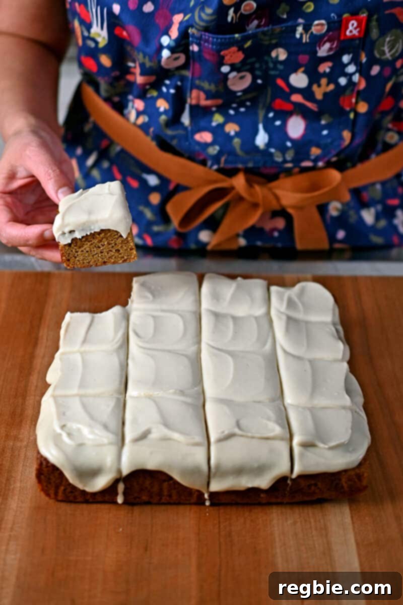Guilt Free Paleo Pumpkin Bars 3 A person in an apron carefully lifting a perfectly baked paleo pumpkin bar, adorned with a swirl of vegan cream cheese frosting.