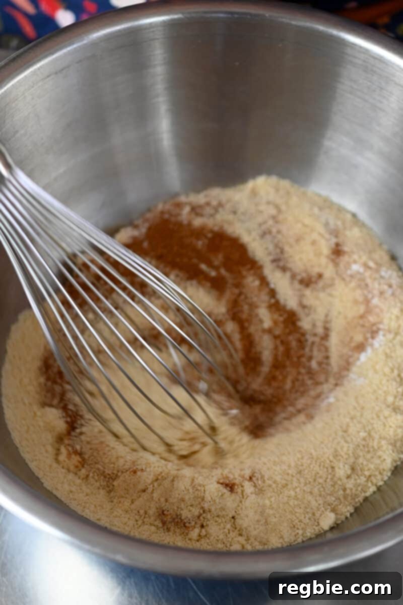 Guilt Free Paleo Pumpkin Bars 6 A closeup of the dry ingredients for paleo pumpkin bars being meticulously whisked together in a large metal mixing bowl.