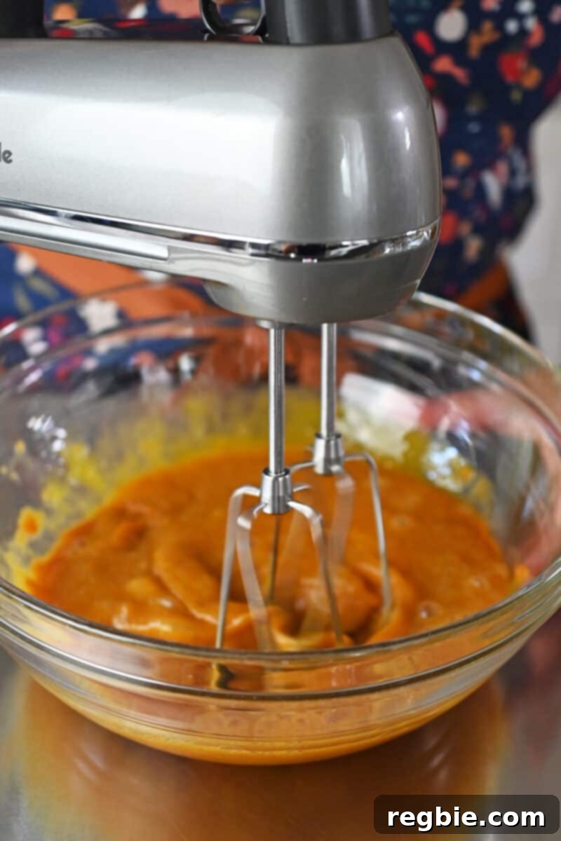 Guilt Free Paleo Pumpkin Bars 7 Using a hand mixer to smoothly combine the wet ingredients for paleo pumpkin bars in a clear glass bowl, ensuring uniformity.