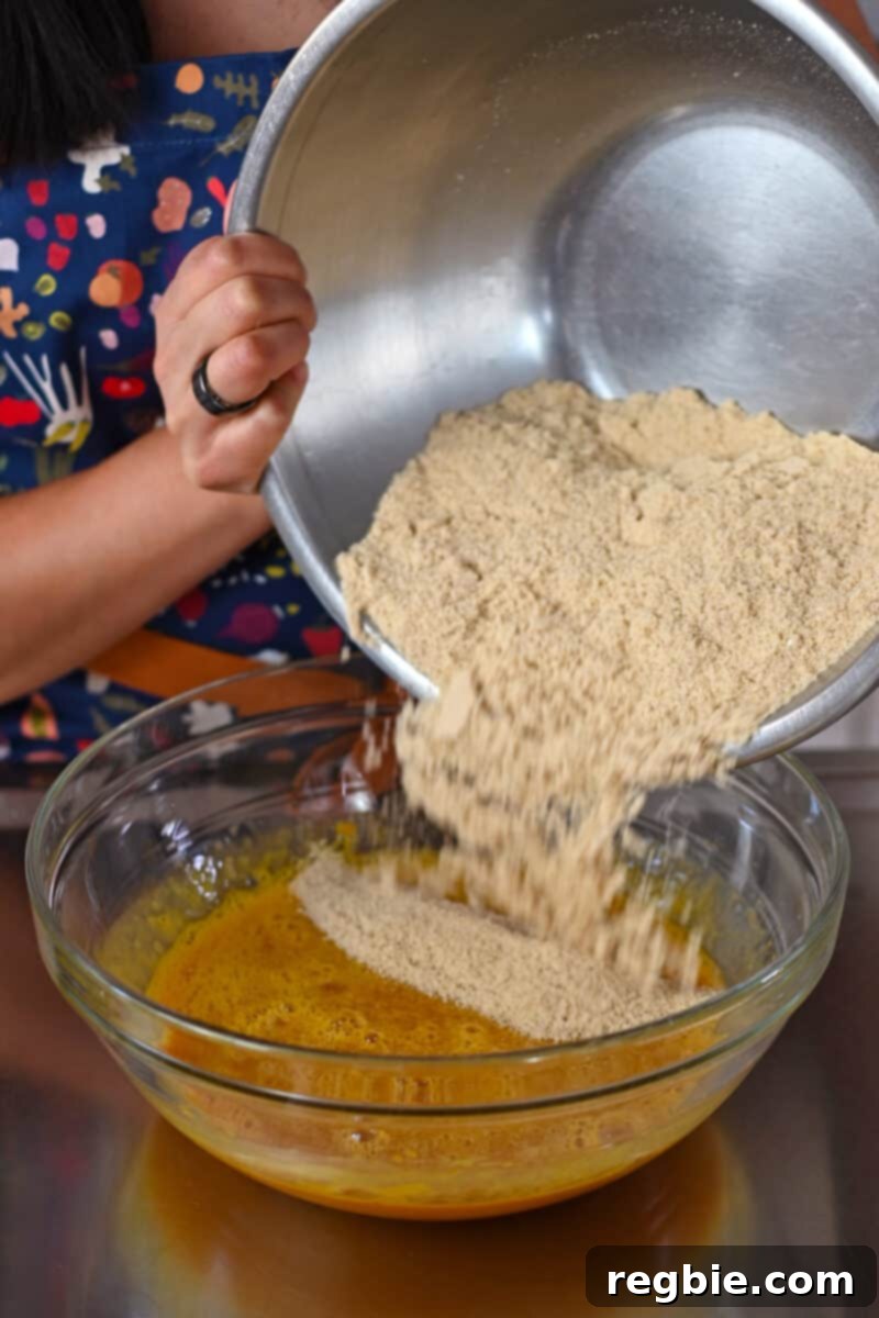 Guilt Free Paleo Pumpkin Bars 8 Pouring the meticulously prepared dry ingredients into the bowl of wet ingredients, ready for combining.