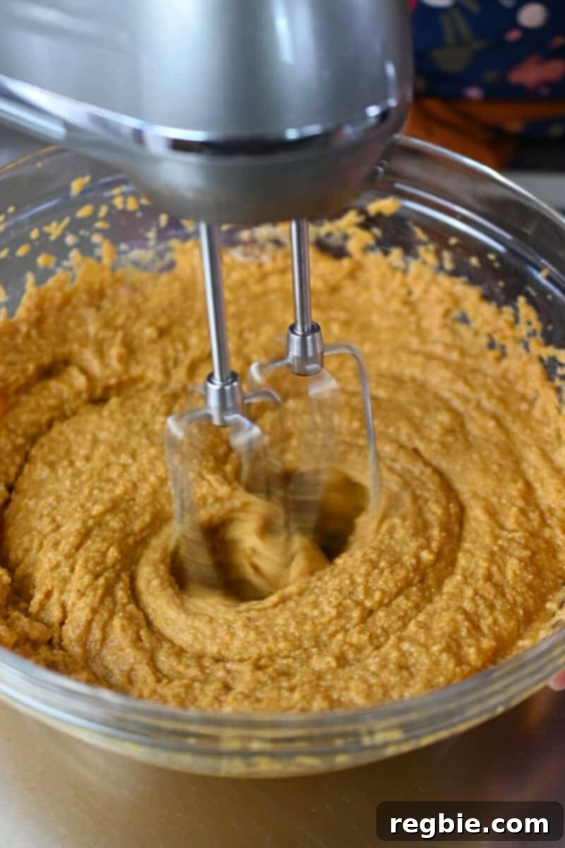 Guilt Free Paleo Pumpkin Bars 9 A hand mixer is gently blending the batter for paleo and gluten free pumpkin bars, ensuring all ingredients are well combined.