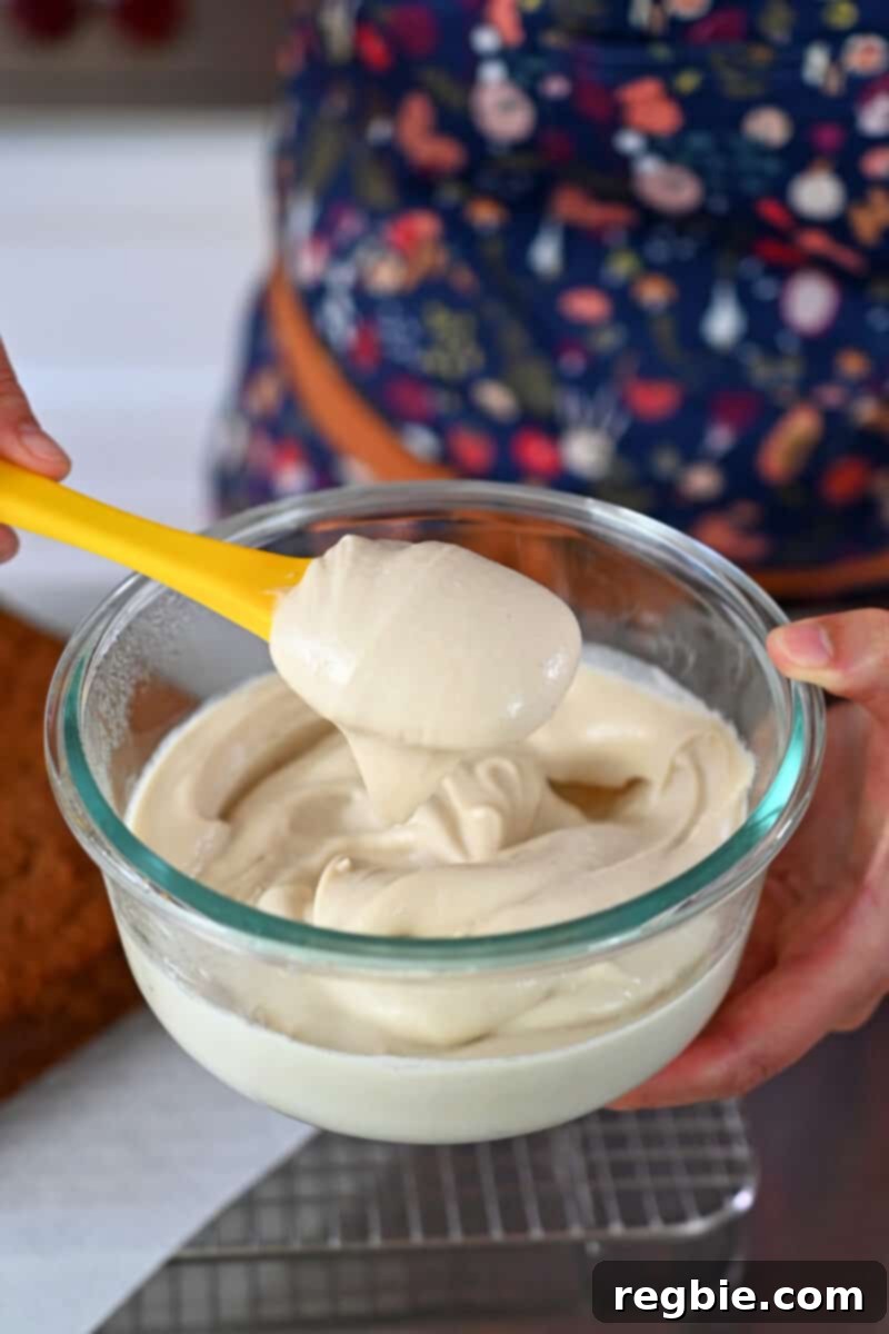 A spatula dipped in luscious dairy-free paleo and vegan cream cheese frosting in a clear glass bowl.