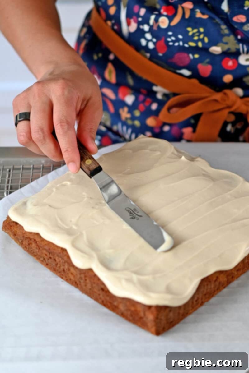 Spreading smooth vegan cream cheese frosting on a delightful square pumpkin cake, ready to enjoy.