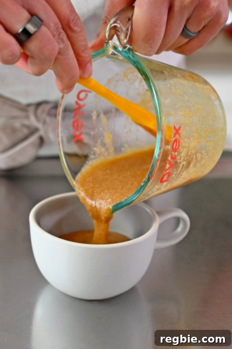 Pouring the perfectly mixed gluten-free mug cake batter into a small, microwave-safe coffee cup, ready for cooking.