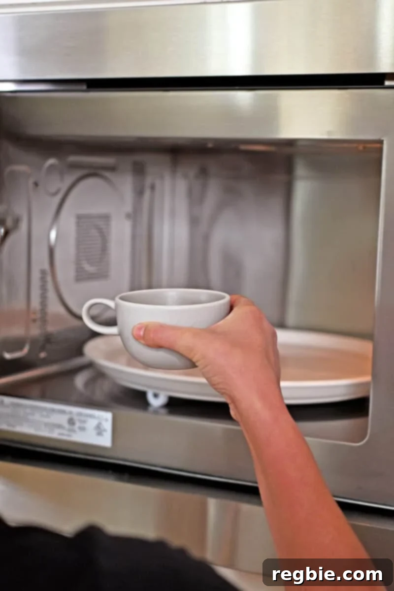 Placing a coffee mug filled with gluten-free apple cake batter precisely in the center of a microwave with a turntable, ready for cooking.