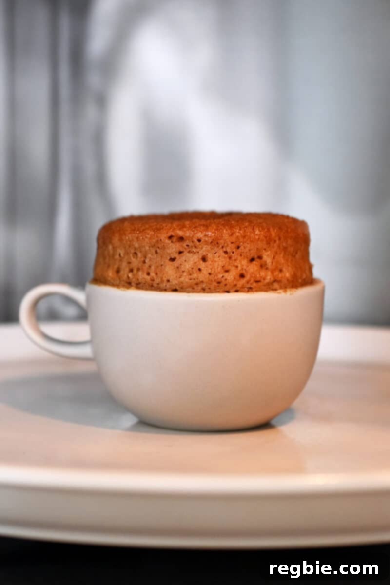 A fully cooked, golden-brown apple mug cake inside a microwave, proudly risen about an inch above the rim of the mug, signifying it's perfectly done.