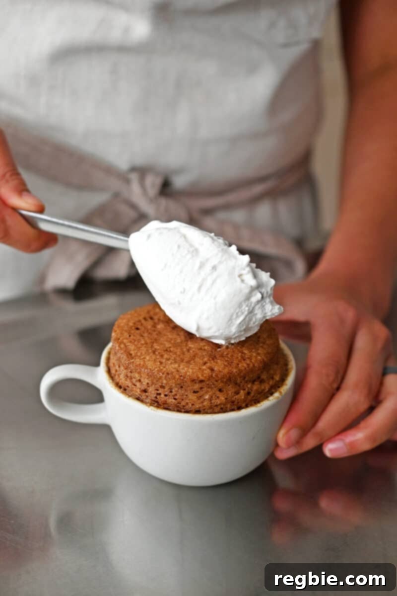 Adding a spoonful of fluffy whipped coconut cream delicately on top of a warm gluten-free apple mug cake.