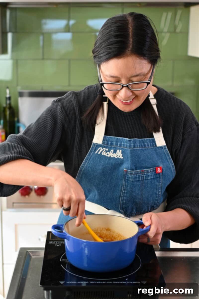 Healthy & Delicious Tonkatsu Sauce (Paleo, Whole30, Vegan) 9 A smiling Asian woman stirring homemade Tonkatsu Sauce simmering in a blue saucepan, ensuring even cooking and thickening.