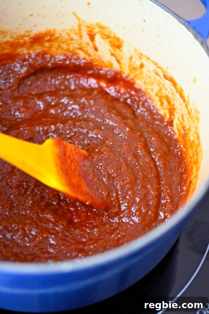 Healthy & Delicious Tonkatsu Sauce (Paleo, Whole30, Vegan) 10 An overhead shot of a thick, simmering reddish brown sauce in a small saucepan, showing the achieved consistency.