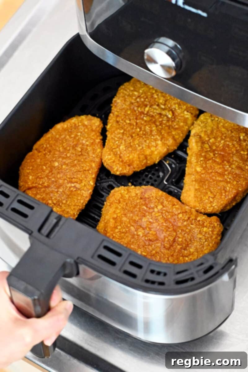 An open air fryer with uncooked tonkatsu inside, being sprayed with avocado oil for a crispy crust.