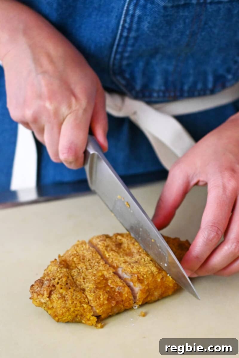 Someone in a blue apron is skillfully slicing up a homemade tonkatsu into even strips, revealing its juicy interior.