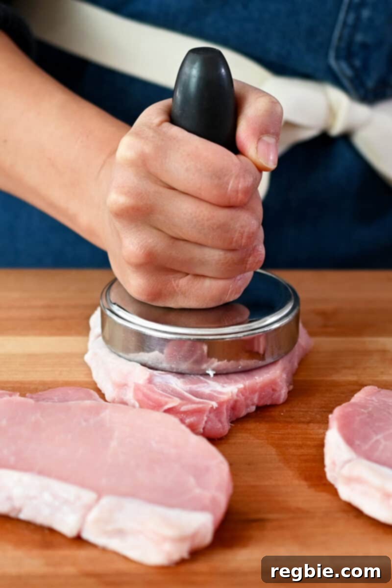 A meat pounder is smashing down on a boneless pork chop to achieve a uniform 1/2-inch thickness.