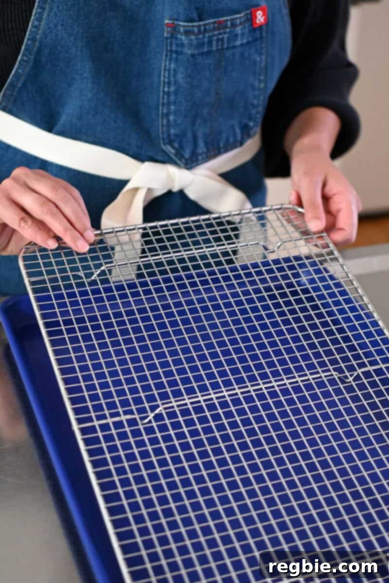 Someone in a denim apron is carefully placing a wire rack inside a blue rimmed baking sheet, preparing it for the breaded pork chops.