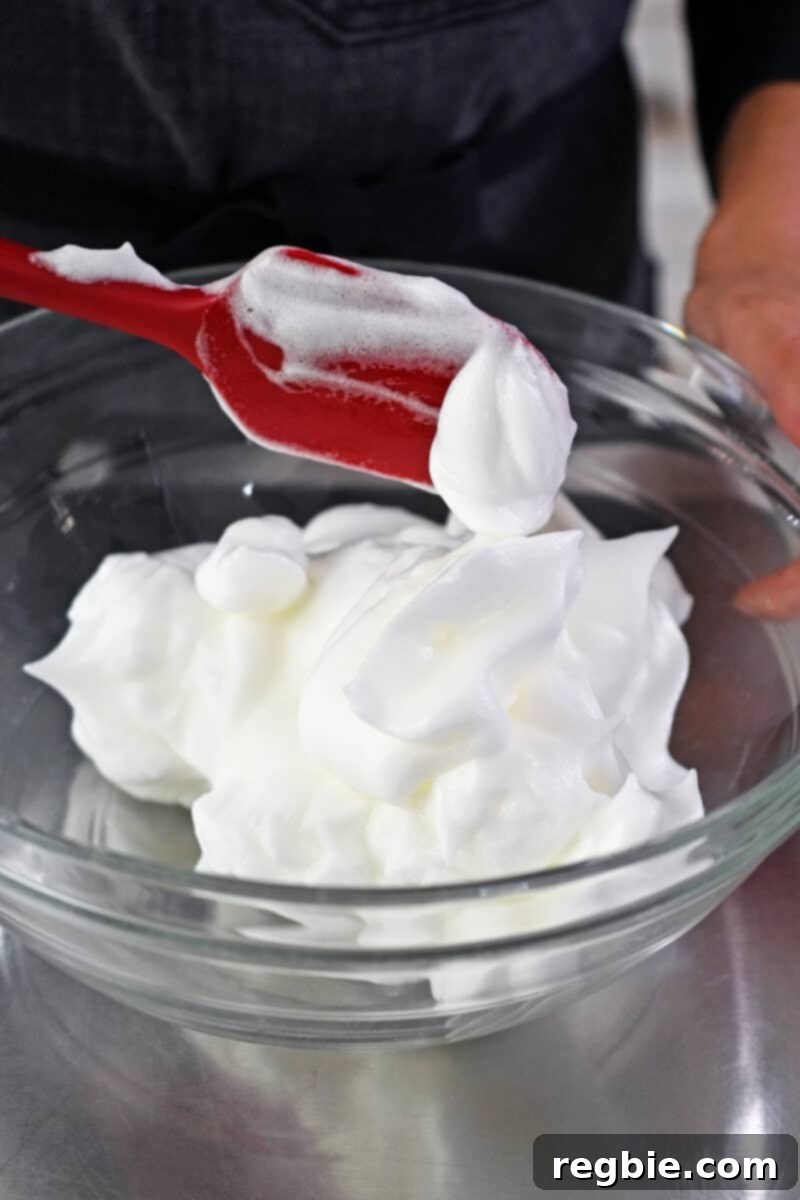 Caprese Chocolate Almond Torte 11 A red silicone spatula is transferring whipped egg whites to a large bowl.