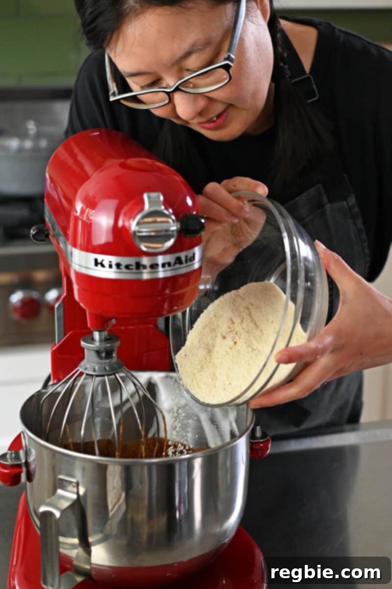 Caprese Chocolate Almond Torte 14 An Asian woman is adding almond flour to a stand mixer filled with Torta Caprese batter.