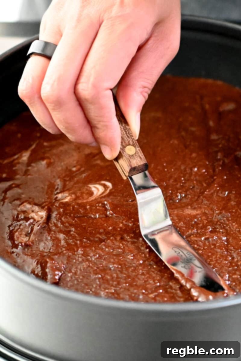 Caprese Chocolate Almond Torte 17 A hand is using an offset spatula to smooth the top of Torta Caprese cake ready for the oven.