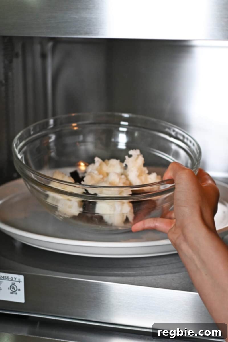 Caprese Chocolate Almond Torte 7 A hand is placing a large glass bowl filled with chopped dark chocolate and coconut oil into a microwave oven.