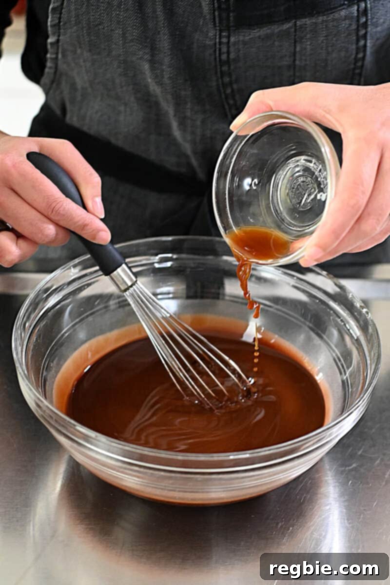 Caprese Chocolate Almond Torte 8 Pouring in a teaspoon of vanilla extract into a bowl of melted chocolate and coconut oil.