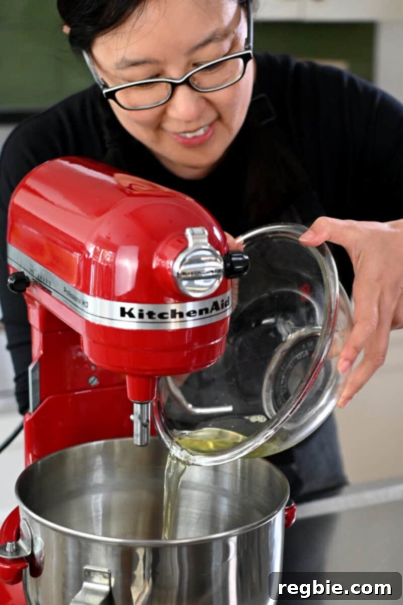Caprese Chocolate Almond Torte 9 A smiling Asian woman in glasses is pouring egg whites into the mixing bowl of a red stand mixer.