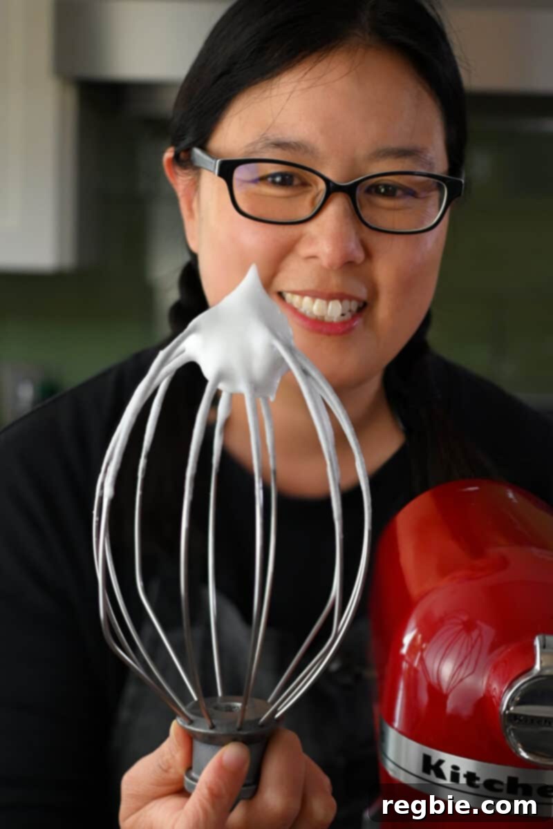 Caprese Chocolate Almond Torte 10 An Asian woman is holding up a whisk that has some whipped egg whites at the tip that are stiff and hold its shape.